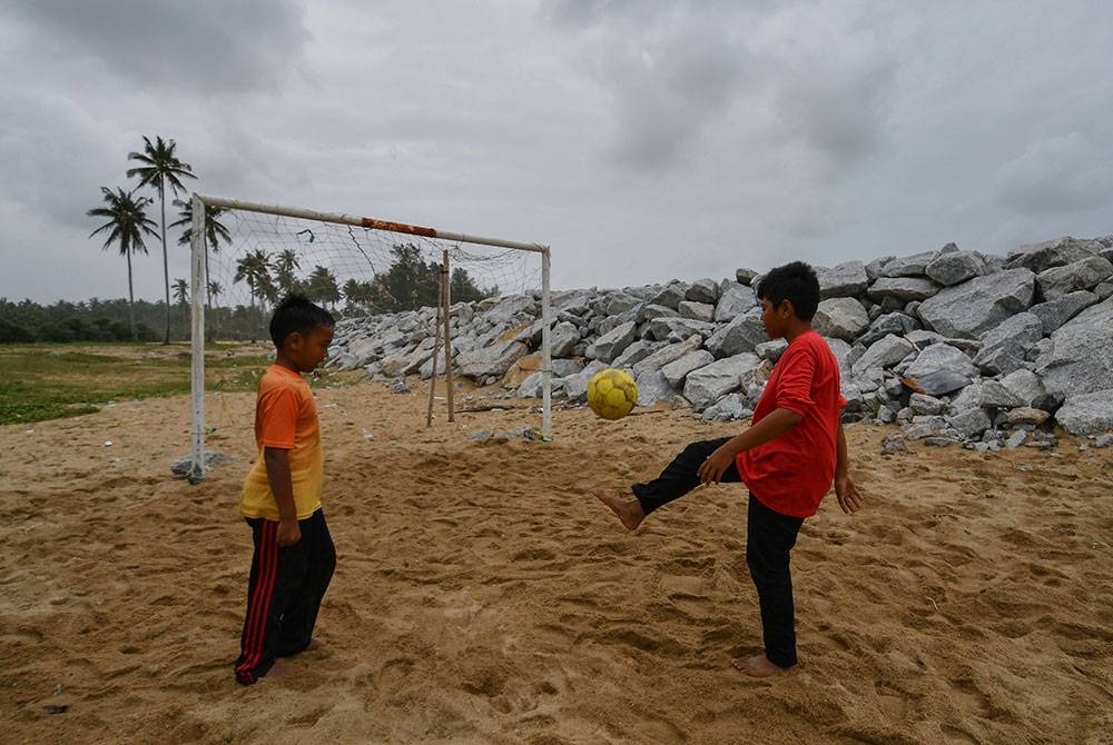 Dua orang kanak-kanak mengambil kesempatan beriadah dengan bermain bola dalam keadaan cuaca mendung berhampiran benteng penahan ombak ketika tinjauan di Pantai Kundur hari ini.