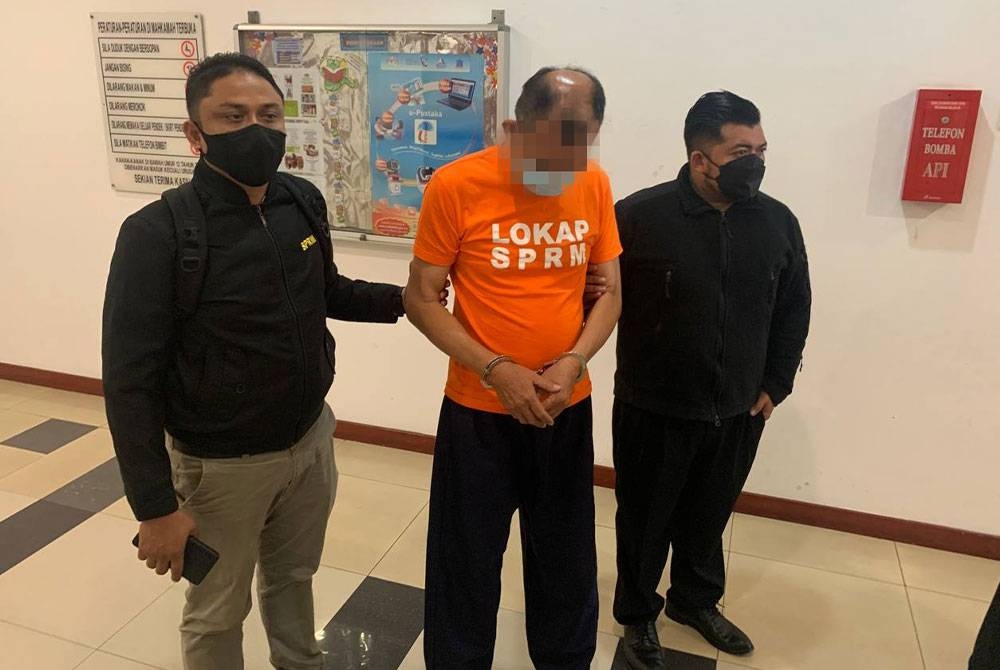 Seorang pengarah syarikat perindustrian (tengah) yang memakai baju lokap SPRM bewarna oren direman lima hari oleh Mahkamah Majistret Shah Alam pada Khamis, bagi membantu siasatan kes menawarkan rasuah RM50,000 kepada seorang pegawai polis.