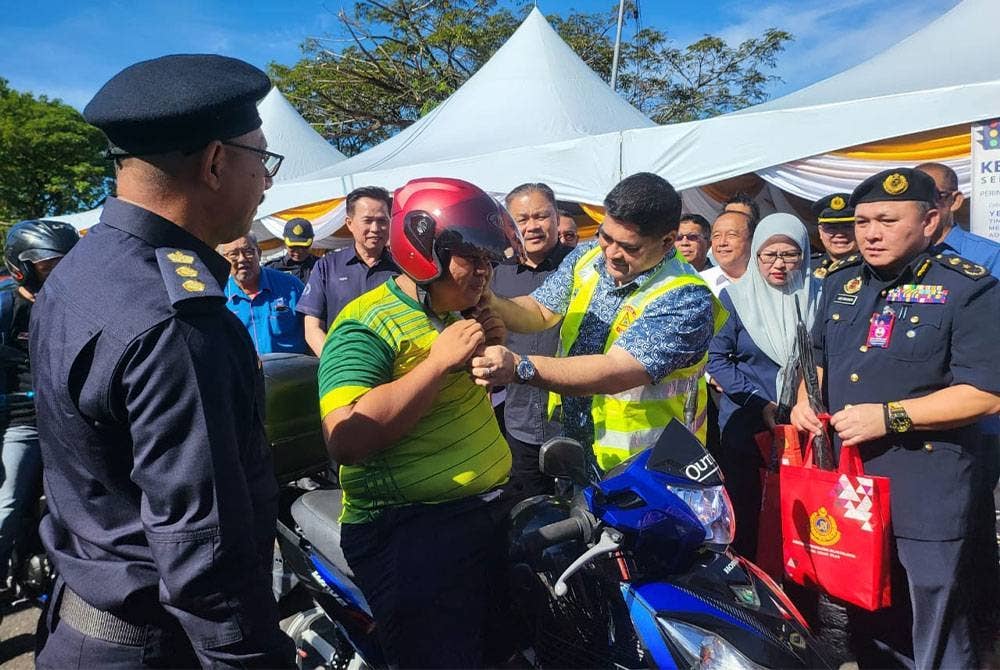 Shahelmey menyampaikan topi keledar kepada penunggang motosikal ketika hadir Program Kesedaran Keselamatan Jalan Raya Sempena Sambutan Perayaan Tahun Baru Cina Peringkat Sabah, di Teluk Dumpil, di Putatan.