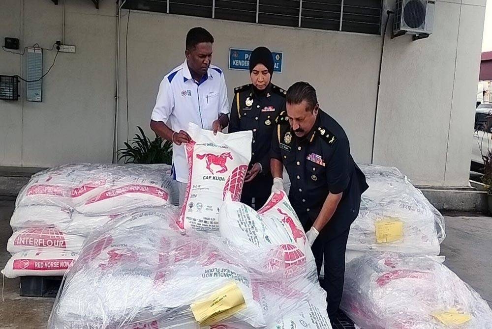 Jegan (kiri) melihat tepung yang dirampas dari sebuah kilang roti terkemuka di Jalan Transfer, Georgetown pada Rabu.