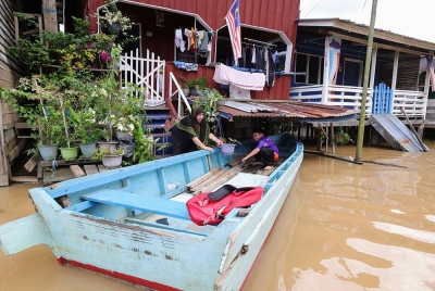 Seorang penduduk mengalihkan pokok hiasan rumah ke tempat lebih tinggi selepas kediaman mereka di Kinabatangan dinaiki air. - Foto: Bernama