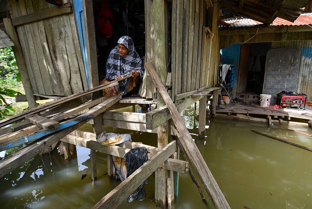 Penduduk setempat Sawiyah Umat, 70, membaiki laluan untuk memudahkannya keluar dari kediaman selepas digenangi banjir ketika tinjauan di Kampung Tersang, Rantau Panjang hari ini.