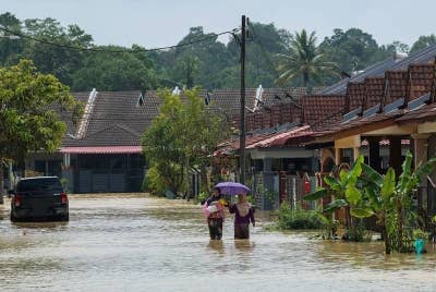 Penduduk Kampung Gudang Rasau, Mariani Mansor, 32, (kiri) bersama kakaknya, Suzana Ismail, 51, meredah banjir sambil mendukung bayinya yang berusia dua bulan ketika meninjau keadaan rumah yang terletak di belakang Taman Seri Damai Perdana pada Selasa. - Foto Bernama