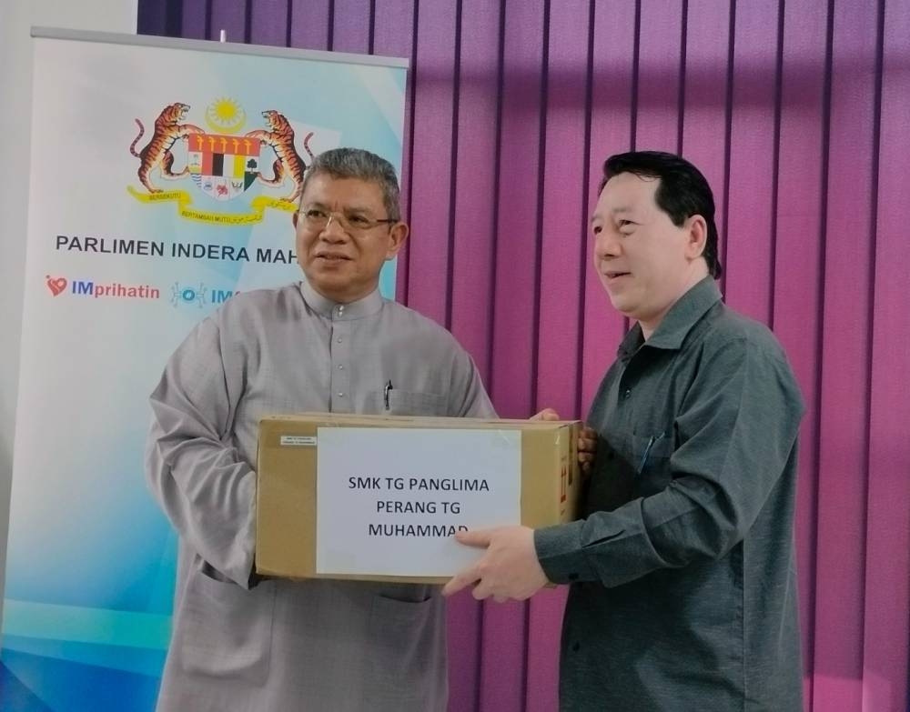 Saifuddin (kiri) menyerahkan buku dan alat tulis kepada wakil guru Sekolah Menengah Kebangsaan kawasan Parlimen Indera Mahkota di pejabat Pusat Khidmat Ahli Parlimen Indera Mahkota, pada Jumaat.