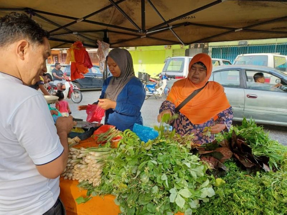 Fauziah (kanan) melayan pelanggan yang mahu beli sayur maman di Pasar Tani Gemencheh, di sini, hari ini.