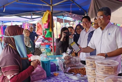 Marzunisham (kanan) menggunakan pembayaran tanpa tunai ketika membeli barang jualan di Pasar Pekan Sehari Jeniang di Kedah pada Isnin.