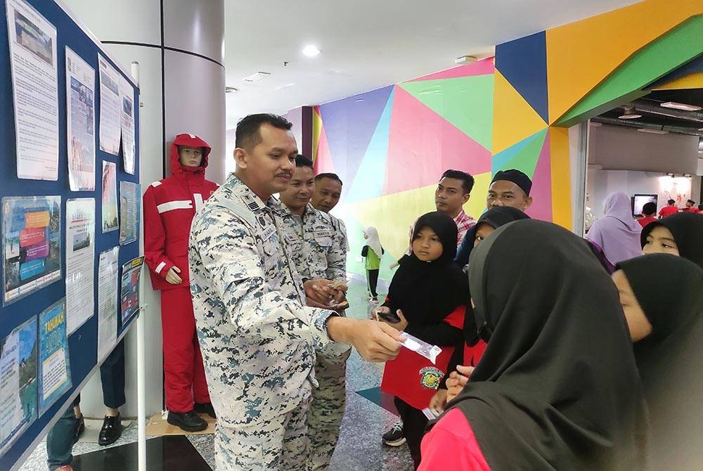 Khairulanuar (kiri) memberi cenderahati kepada murid yang mengambil bahagian dalam aktiviti dijalankan sempena pameran sempena Sambutan Hari Ulang Tahun Maritim Malaysia ke-18 di Pusat Sains dan Kreativiti Terengganu (PSKT), di sini pada Rabu.