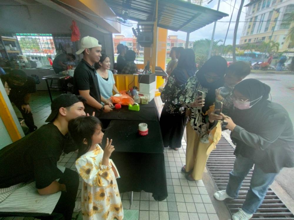 Adib (kiri) melayan pelanggan yang datang ke kedainya di Bandar Kajang.