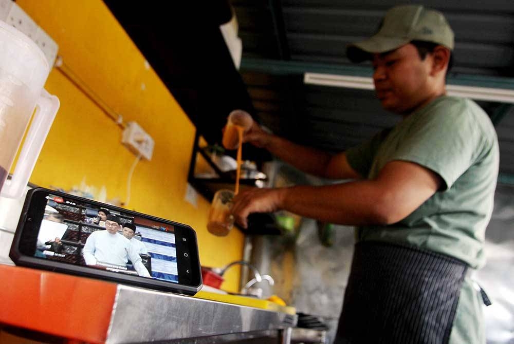 Peniaga Ahmad Muzakkir Ahmad Zabri, 30, mengikuti siaran langsung pembentangan Belanjawan 2023 oleh Perdana Menteri yang juga Menteri Kewangan Datuk Seri Anwar Ibrahim melalui telefon pintarnya pada tinjauan di kedai makan Ayam Goreng Kunyit Bonggol hari ini.