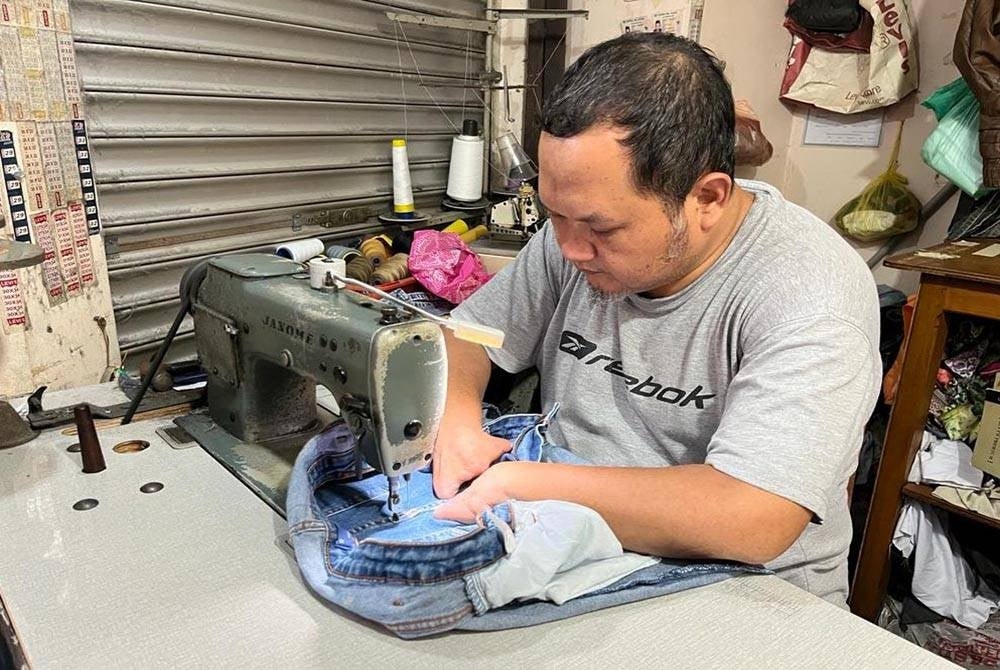 Mohd Alamin menjahit seluar yang dihantar pelanggan.