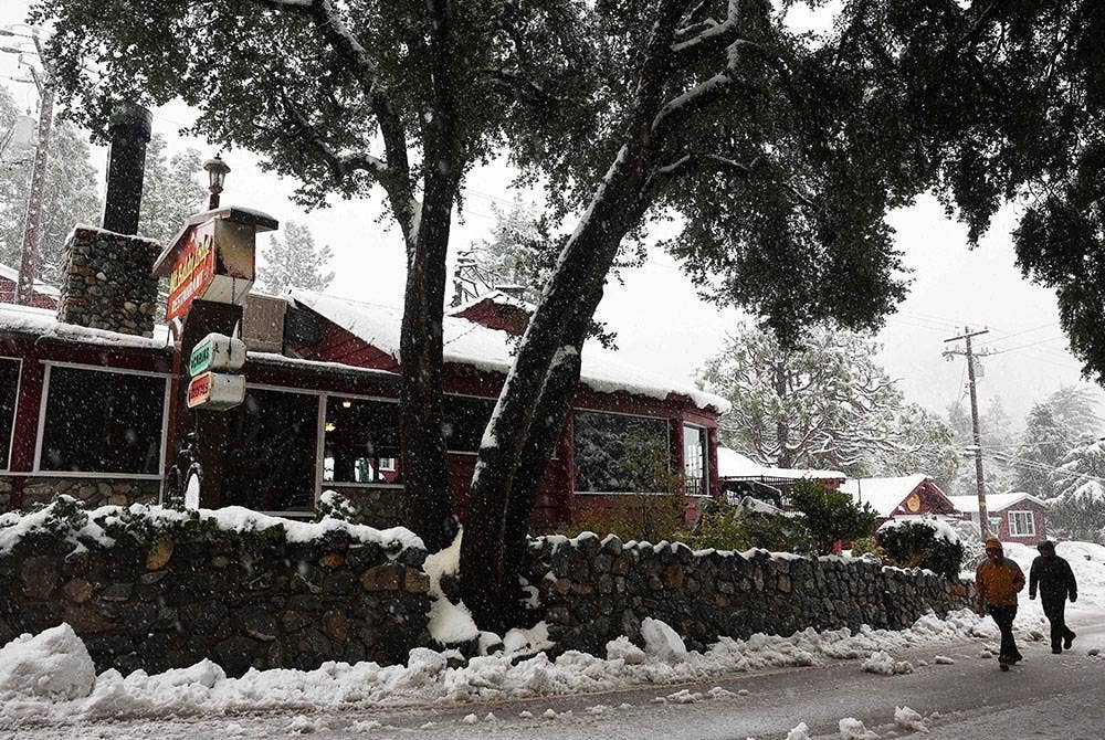 Orang ramai berjalan melepasi sebuah restoran ketika salji turun di Pergunungan San Gabriel berhampiran Los Angeles. - Foto AFP