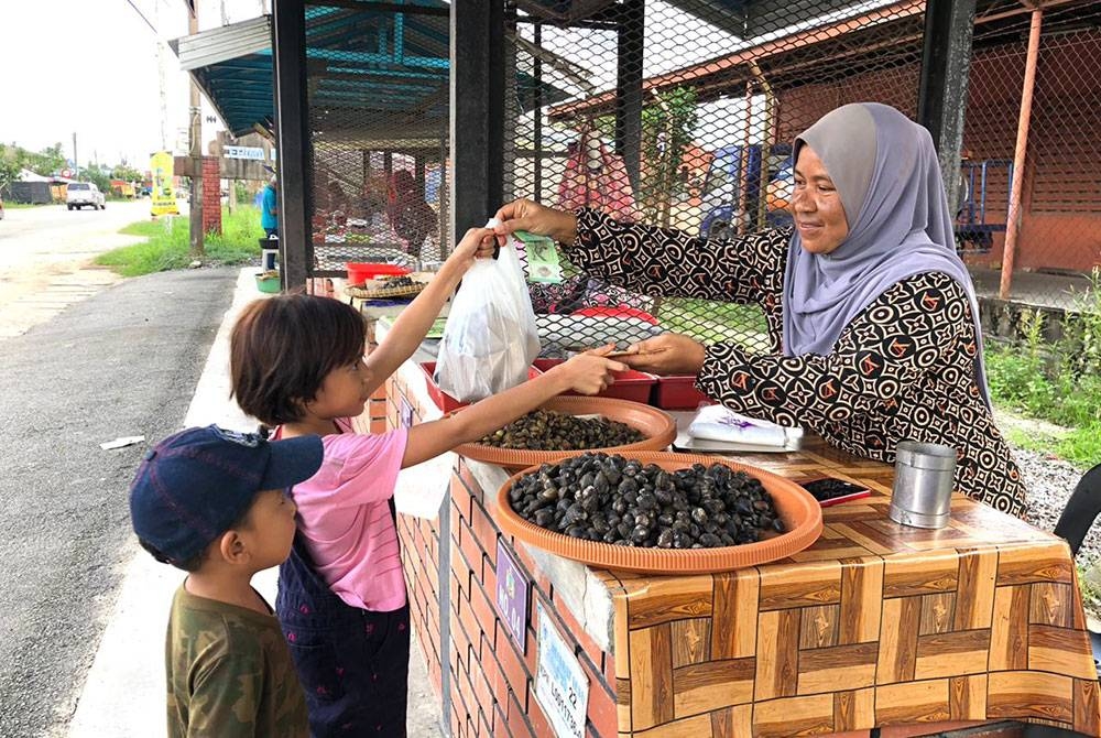 Pelanggan cilik membeli etak yang dijual oleh Norazila (kanan).