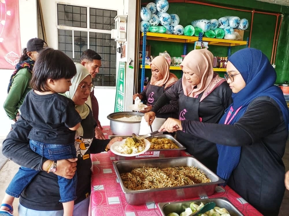 Nuradlin Adlina (kanan) membantu pekerja RMP melayani pengunjung.