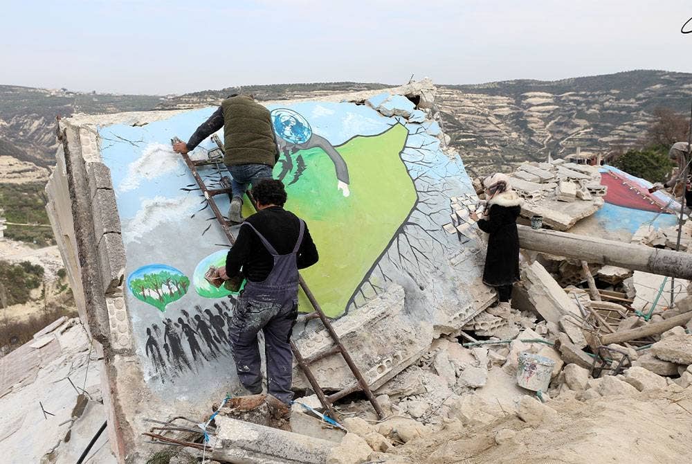 Aziz Asmar, Anees Hamdoun, Bushra Hamed dan Salam Hamed mengecat sekeping dinding bangunan runtuh di kampung Al-Milan di bandar Idlib di Syria pada Sabtu. - Foto EPA