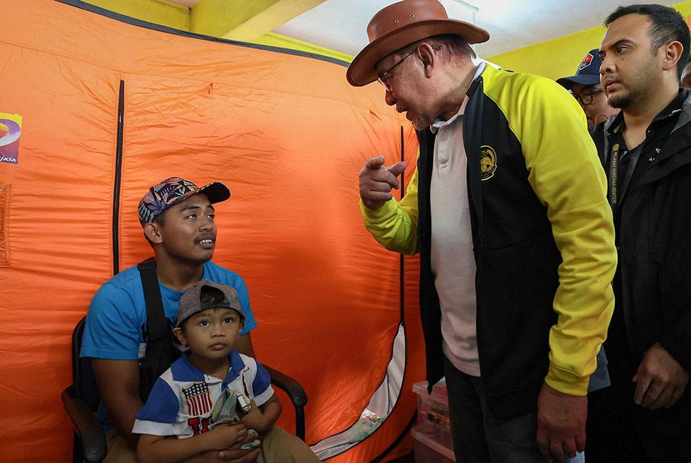 Perdana Menteri Datuk Seri Anwar Ibrahim menyantuni salah seorang mangsa banjir ketika turun padang meninjau situasi banjir di Pusat Pemindahan Sementara (PPS) Sekolah Kebangsaan Gemereh hari ini. - Foto Bernama