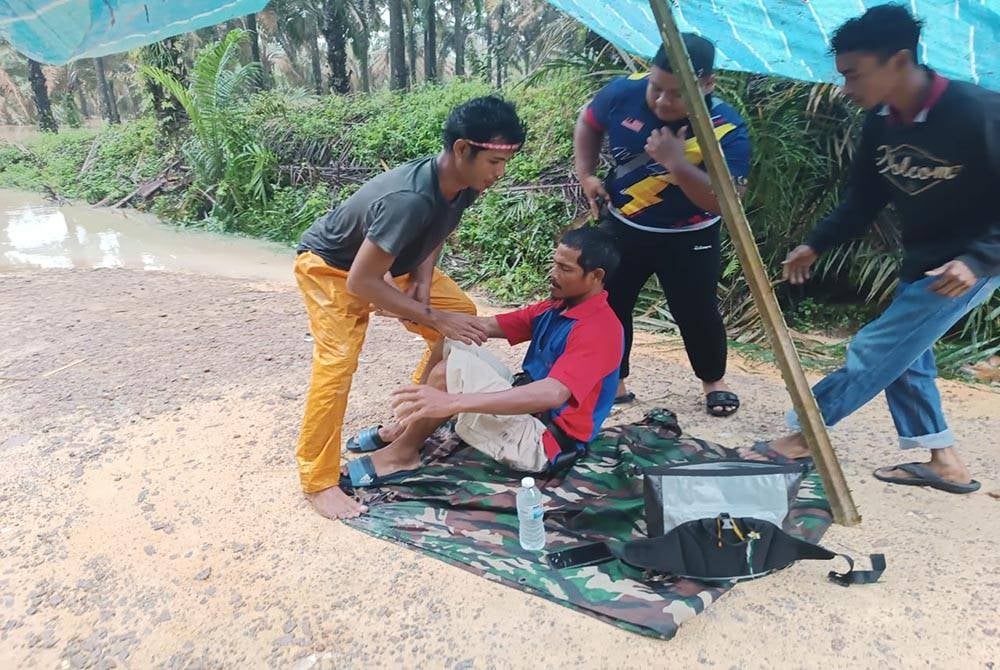 Mangsa (duduk) yang cedera akibat diserang buaya dibantu penduduk kampung mendapatkan rawatan di Klinik Kesihatan Kahang pada Ahad.