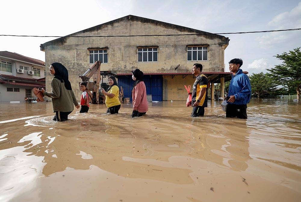 Sebuah keluarga terpaksa meredah banjir untuk pergi melihat keadaan kediaman ketika tinjauan di Seri Medan Batu Pahat pada Ahad. - Foto Bernama