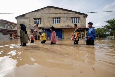 Sebuah keluarga terpaksa meredah banjir untuk pergi melihat keadaan kediaman ketika tinjauan di Seri Medan Batu Pahat pada Ahad. - Foto Bernama