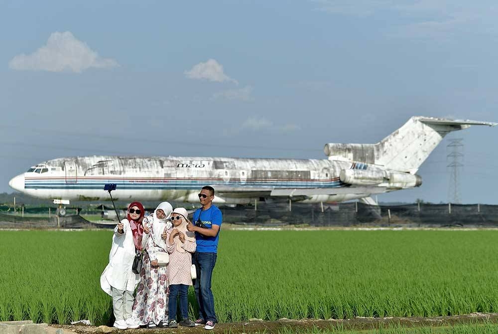Pengunjung Rosli Jaafar, 50, (kanan) dan isteri Azlina Mohd Sidik, 42, (kiri) berswafoto bersama anak-anak sambil menikmati keindahan pemandangan sawah padi berlatar belakangkan sebuah kapal terbang yang tidak digunakan lagi. 