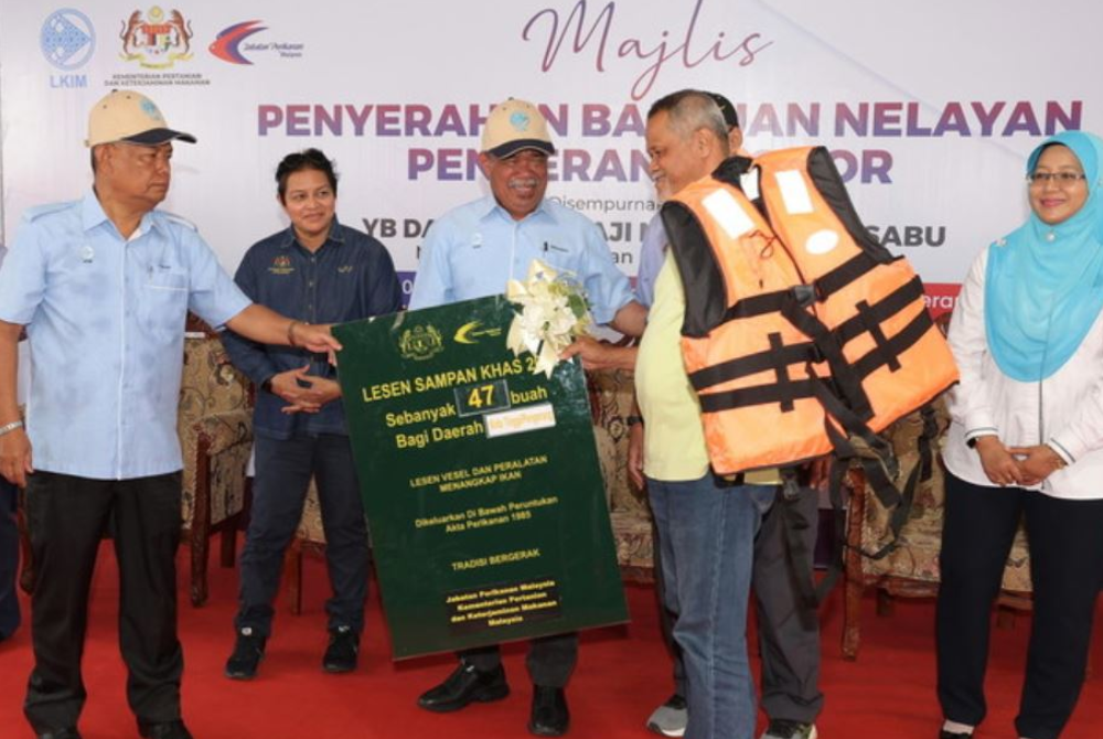 Mohamad (tiga, kiri) menyerahkan lesen sampan khas dan jaket keselamatan kepada wakil Ketua Jaringan Perikanan Sungai Rengit, Razak Nahar (dua, kanan) pada Majlis Penyerahan Bantuan Kepada Nelayan di Kompleks LKIM, Pengerang pada Rabu. - Foto Bernama