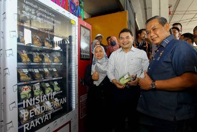 Rafizi (dua dari kiri) dan Aminuddin menunjukkan makanan yang dibeli di mesin layan diri IPR.