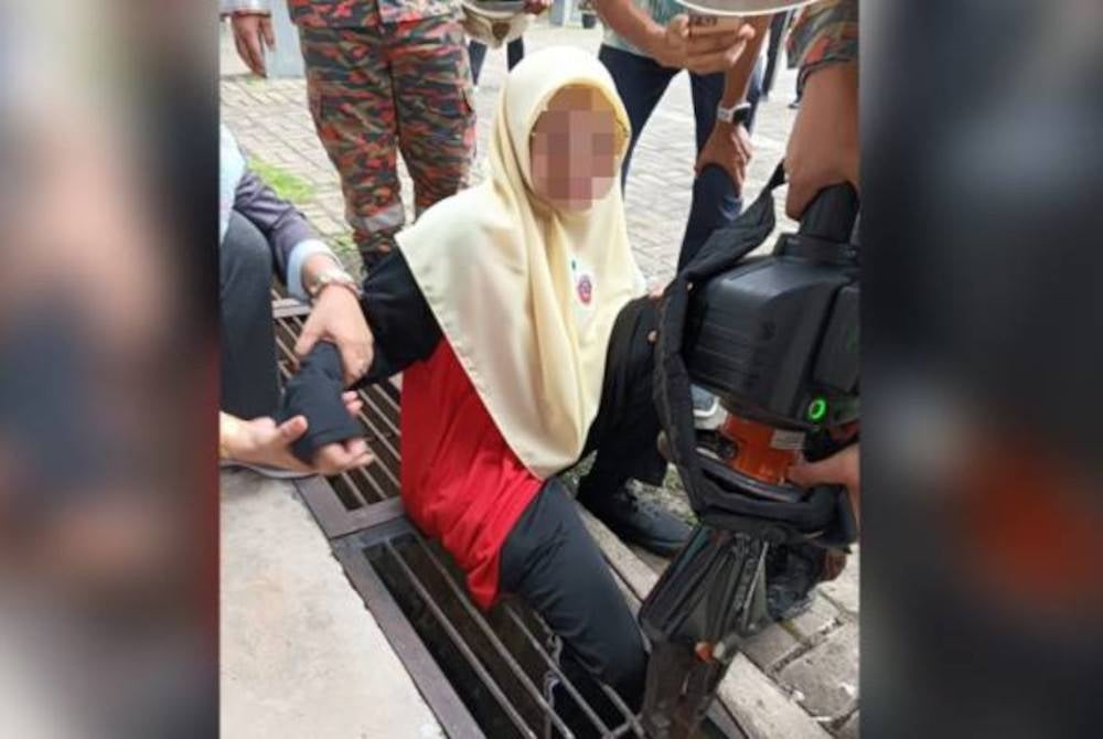 Keadaan pelajar yang terjatuh dan tersepit pada besi penutup longkang selama 20 minit sebelum berjaya diselamatkan pihak bomba. - Foto JBPM