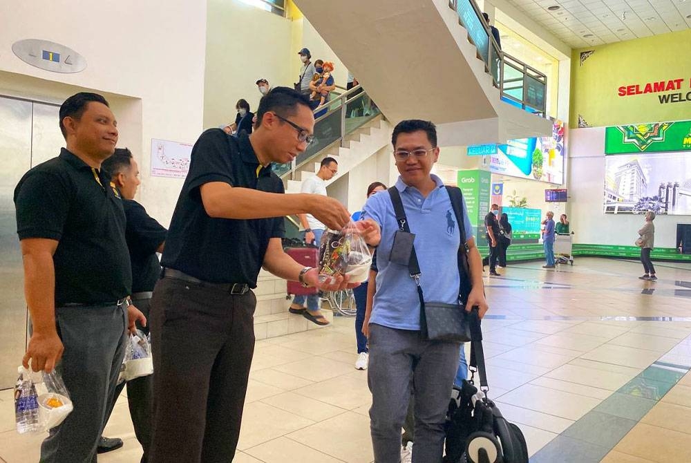 Mohd Iqmal (dua dari kiri) mengagihkan bubur lambuk kepada perantau yang tiba di Lapangan Terbang Sultan Ismail Petra, Kota Bharu pada Khamis.