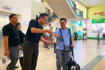 Mohd Iqmal (dua dari kiri) mengagihkan bubur lambuk kepada perantau yang tiba di Lapangan Terbang Sultan Ismail Petra, Kota Bharu pada Khamis.