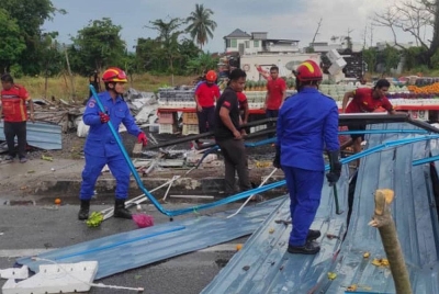 Anggota APM Kubang Pasu membersihkan bumbung diterbangkan angin hingga menutup jalan di jalan utama Jitra-Changlun pada Khamis.