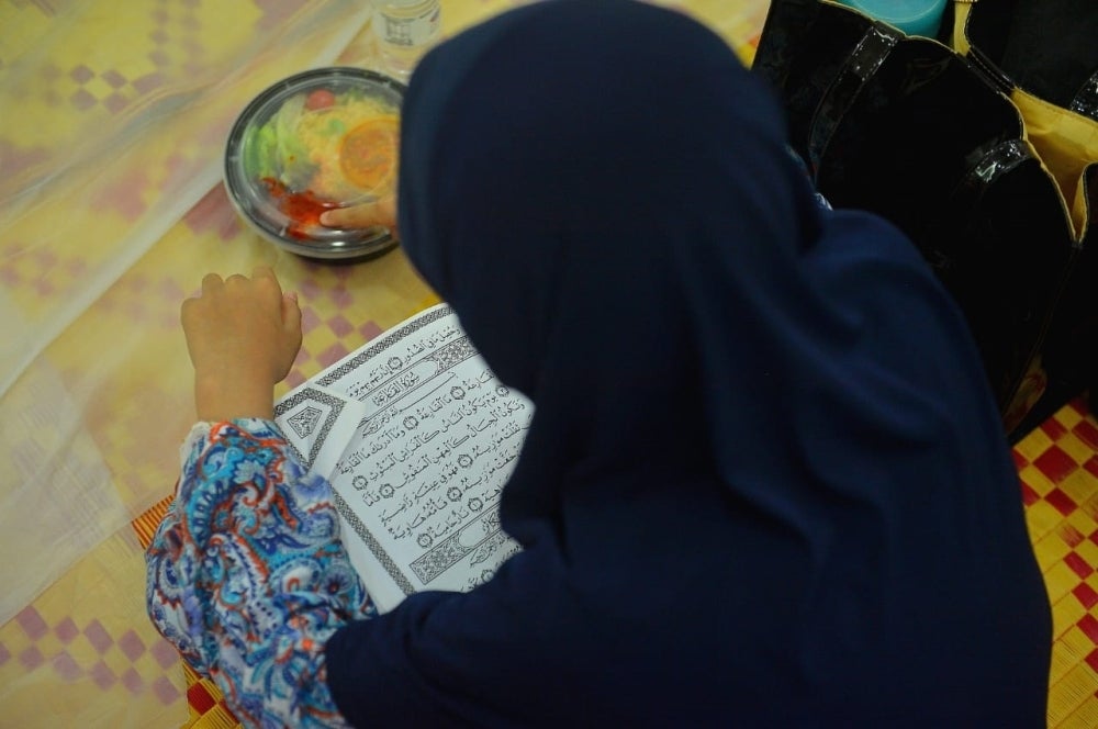 Seorang pengunjung memanfaatkan waktu dengan mengaji al-Quran ketika menanti waktu berbuka puasa.