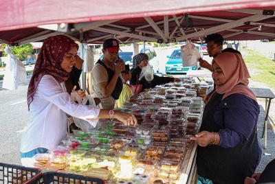 Pembantu Kedai, Nurul Nartisa Ishak (kanan) melayan pelanggan untuk membeli pelbagai kuih muih yang dijual pada harga RM1 sepaket di sebuah gerai di Taman Klebang Restu pada Jumaat. - Foto Bernama