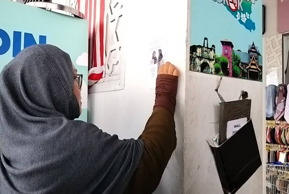 Noor Fatimahtul Zaharah menampalkan poster gambar anaknya Aliah Qistina di Jasin Bestari di sini, pada Isnin.