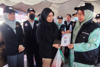 Dr Kasemani (kanan) memberi penerangan tentang kos imbasan QR yang diwujudkan JKNT kepada seorang pengunjung bazar Ramadan Gong Badak, Kuala Nerus pada Ahad.