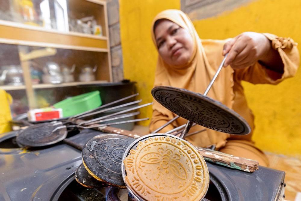 Noriah sedang membakar kuih kapit ketika ditemui di rumahnya di Kampung Pulau Suri. - Foto Bernama