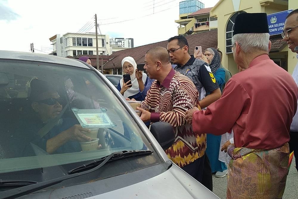 Saarani (tiga dari kanan) menyerahkan bubur lambuk kepada orang ramai yang melalui kawasan Rumah Pangsa Jalan Ashby, Ipoh pada Khamis.