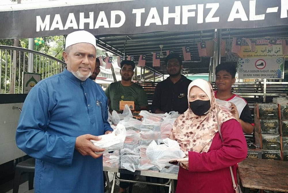 Jawahar (kiri) menyampaikan kurma kepada mereka yang hadir mengisi borang permohonan bantuan Hari Raya di Tahfiz Al-Madrasathul Faridiyah di Taman Sri Rampai pada Ahad.