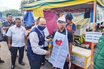 Dr Othman memakaikan apron kepada peniaga bazar Ramadan ketika pemeriksaan dan operasi kebersihan serta keselamatan makanan di Bazar Ramadan Taman Sri Aman di sini pada Isnin.
