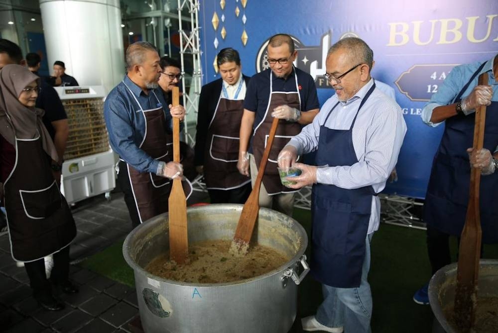 Mohammad Hanis (kanan) mengetuai program menyediakan bubur lambuk yang diadakan di Bank Rakyat.