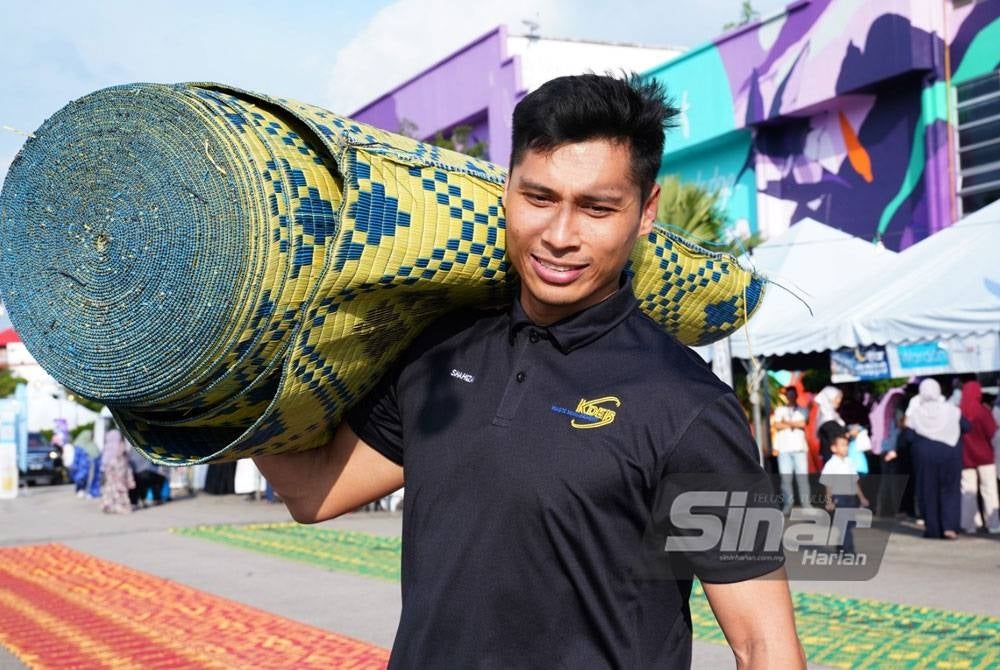 Seorang pekerja KDEBWM mengangkat tikar untuk dibentangkan sebelum majlis berbuka puasa.