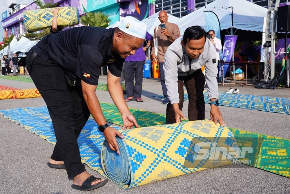 Dua pekerja KDEBWM melakukan persediaan dengan membentangkan tikar sebelum majlis berbuka puasa.