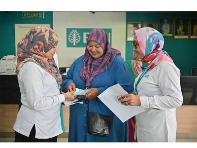 Nozilawati ( tengah) menerima wang tunai STR sebanyak RM200 selepas selesai proses penunaian di BSN Cawangan Kuala Nerus, pada Rabu.