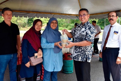 Adly (dua, kanan) mengagihkan bubur lambuk kepada pengunjung. - Foto Bernama