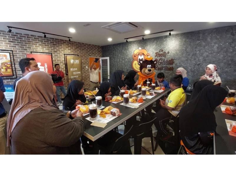 Kakitangan LBS bersama anak-anak yatim dan asnaf serta guru membaca doa berbuka puasa di sebuah kedai makanan segera.