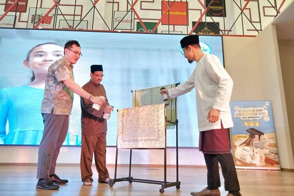 Ustaz Don Daniyal (kanan) menyembur Febreeze Koleksi Inspirasi Attar di sejadah sebagai gimik pelancaran memperkenalkan produk itu di Mydin Mall, Tunjong.