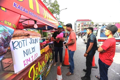 Mohd Tarmimi menyerahkan roti john RM1 kepada pelanggan
