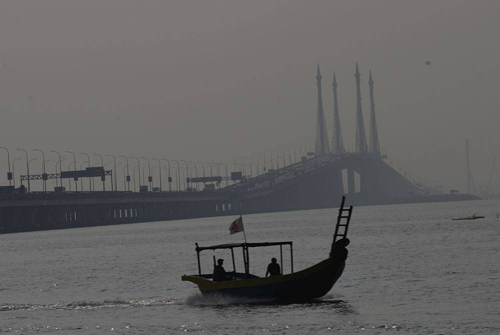 Sebuah bot nelayan melalui berhampiran Jambatan Pulau Pinang yang kelihatan kabur di tengah laut ekoran cuaca berjerebu hari ini.