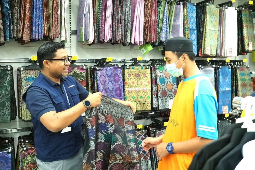 Kakitangan AmanahRaya membantu seorang anak yatim memilih samping di pasar raya Mydin, Seremban pada Selasa.