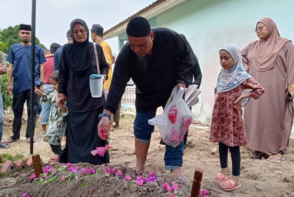 Hermes Latin menabur bunga atas pusara anaknya yang disemadikan di Tanah Wakaf Perkuburan Islam, Kampung Bukit Tunggal, Segamat pada Sabtu.