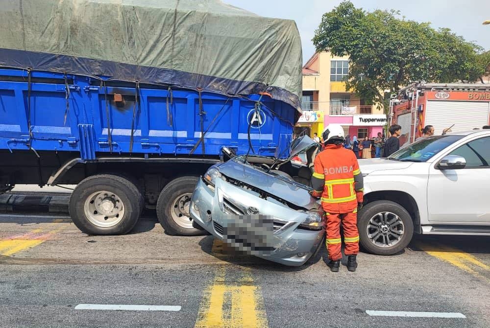 Seorang anggota bomba memerhati sebuah kereta yang remuk teruk selepas dilanggar secara mengundur oleh treler membawa muatan pasir di Rawang Mutiara Business Centre, Rawang, Selangor pada Isnin.
