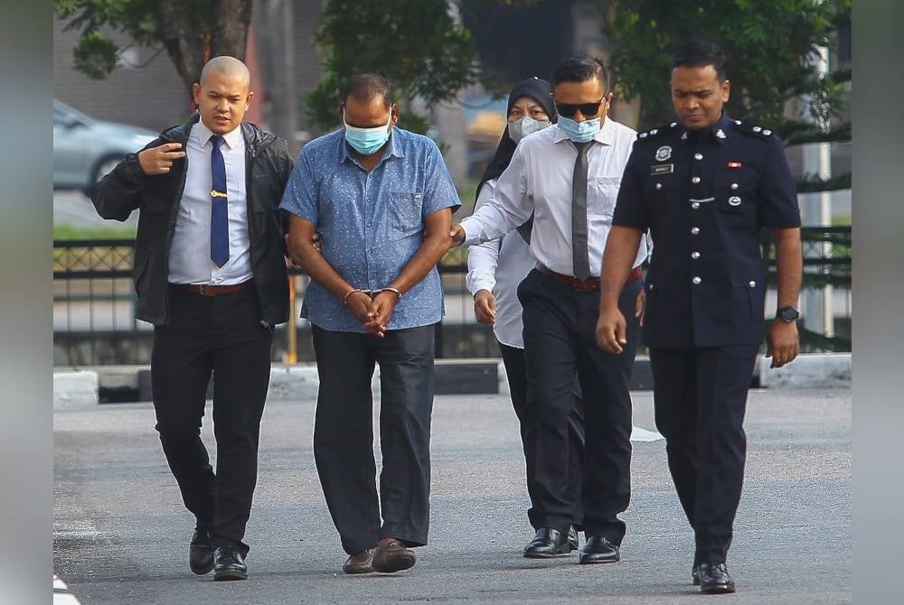 Gunasegaran (dua dari kiri) diiring polis sebaik tiba di mahkamah.